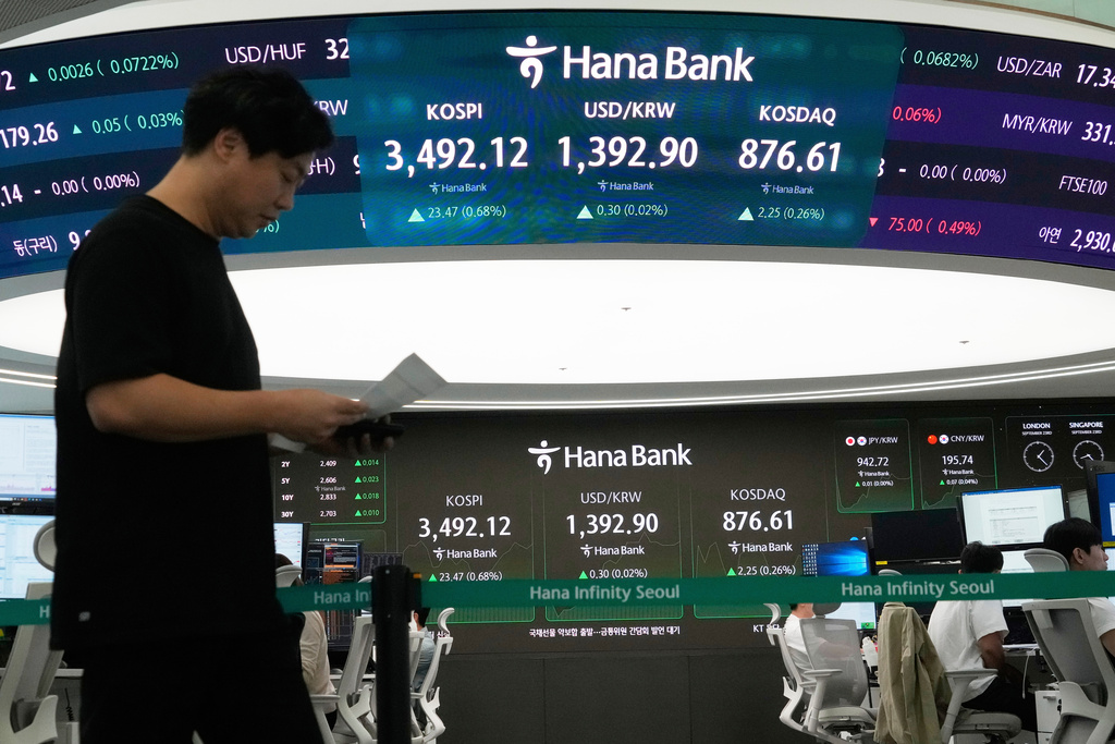  A currency trader passes by a screen showing the Korea Composite Stock Price Index (KOSPI), top center left, and the foreign exchange rate between US dollar and South Korean won, top center, at the foreign exchange dealing room of the Hana Bank headquart